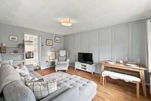 A living room with a sofa, armchair, TV, and a dining table set for two. - Heatherwood Cottage - Central Scone (Scone)