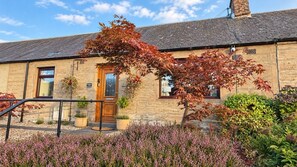 A stone building with a wooden door, potted plants, and a garden with pink flowers. - Heatherwood Cottage - Central Scone (Scone)