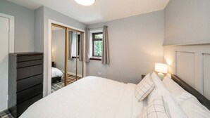 A bedroom with a bed, a dresser, a mirror, and a window with curtains. - Heatherwood Cottage - Central Scone (Scone)