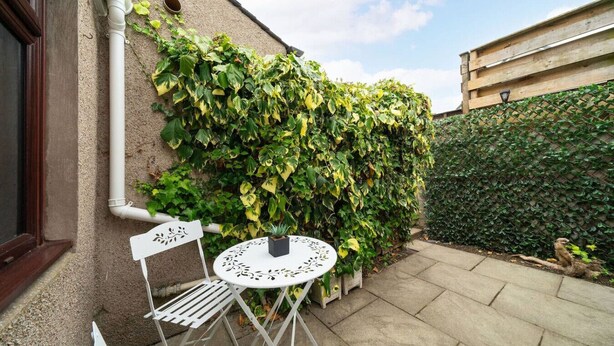 A patio with a white table and chairs, a small potted plant, and a wall covered in green ivy. - Heatherwood Cottage - Central Scone (Scone)