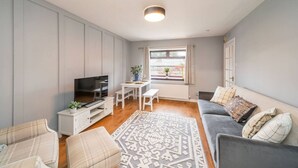 A modern living room with a flat-screen TV, a dining table with chairs, a grey sofa, and a patterned rug. - Heatherwood Cottage - Central Scone (Scone)