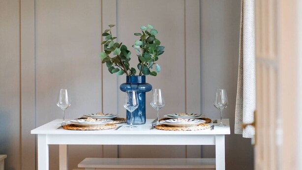 A dining table with plates and glasses, a blue vase with green leaves, and a white bench. - Heatherwood Cottage - Central Scone (Scone)