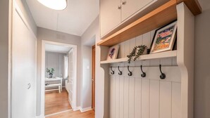 A hallway with a wooden floor, a white door, and a white wall with a shelf holding a framed picture and a plant. - Heatherwood Cottage - Central Scone (Scone)