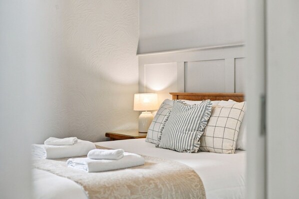 A hotel room with a neatly made bed, a bedside lamp, and a nightstand with a lamp.