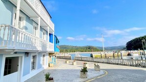 A waterfront building with a balcony, a view of the water, and a hilly landscape in the background.