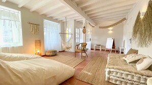 A spacious room with a large bed, a sofa, a hanging chair, and a small table with a whiteboard.