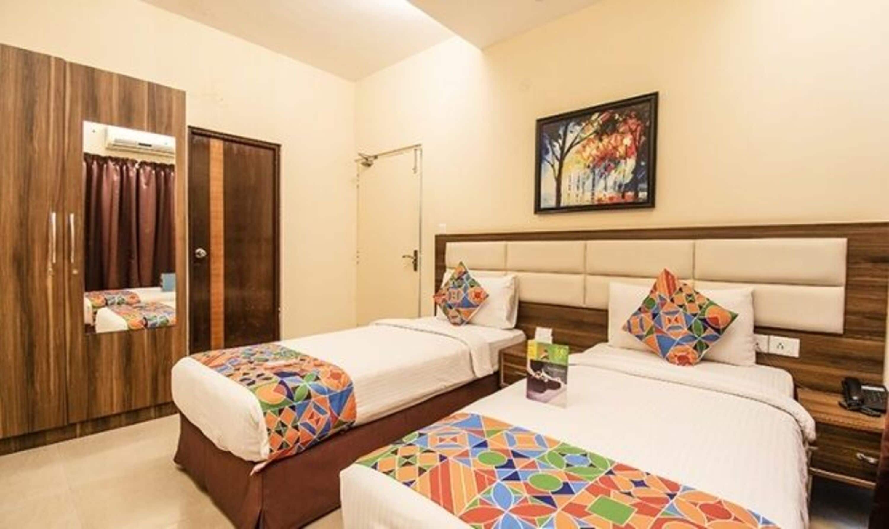 A hotel room with two beds, a wooden wardrobe, a painting on the wall, and a small table with a phone and a bottle.