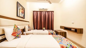 A hotel room with two beds, a ceiling fan, an air conditioning unit, a window with curtains, and a small table with a book. - Fabhotel Celebrity Layout (Bengaluru)