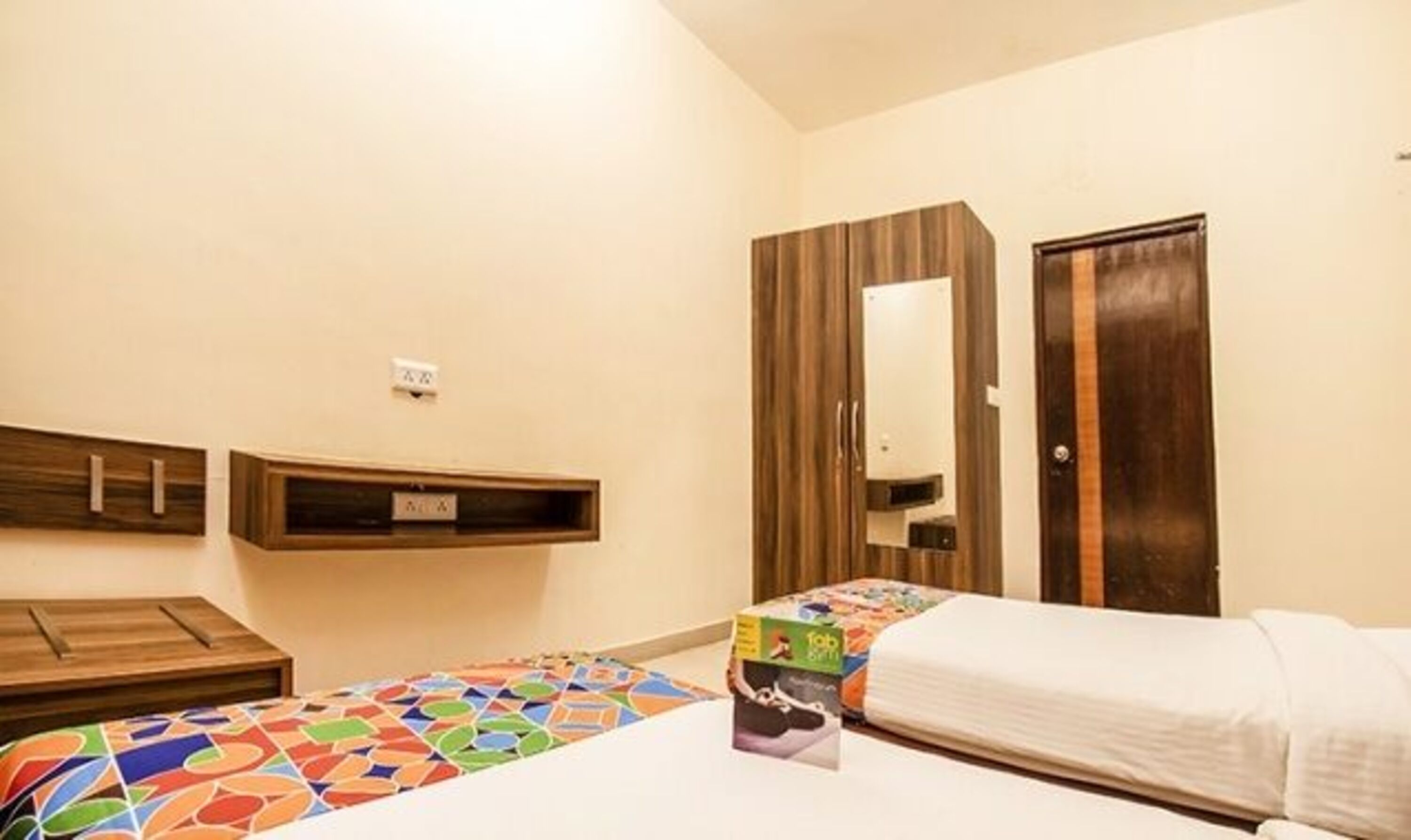 A bedroom with two beds, a wooden wardrobe, a mirror, and a small wooden cabinet.