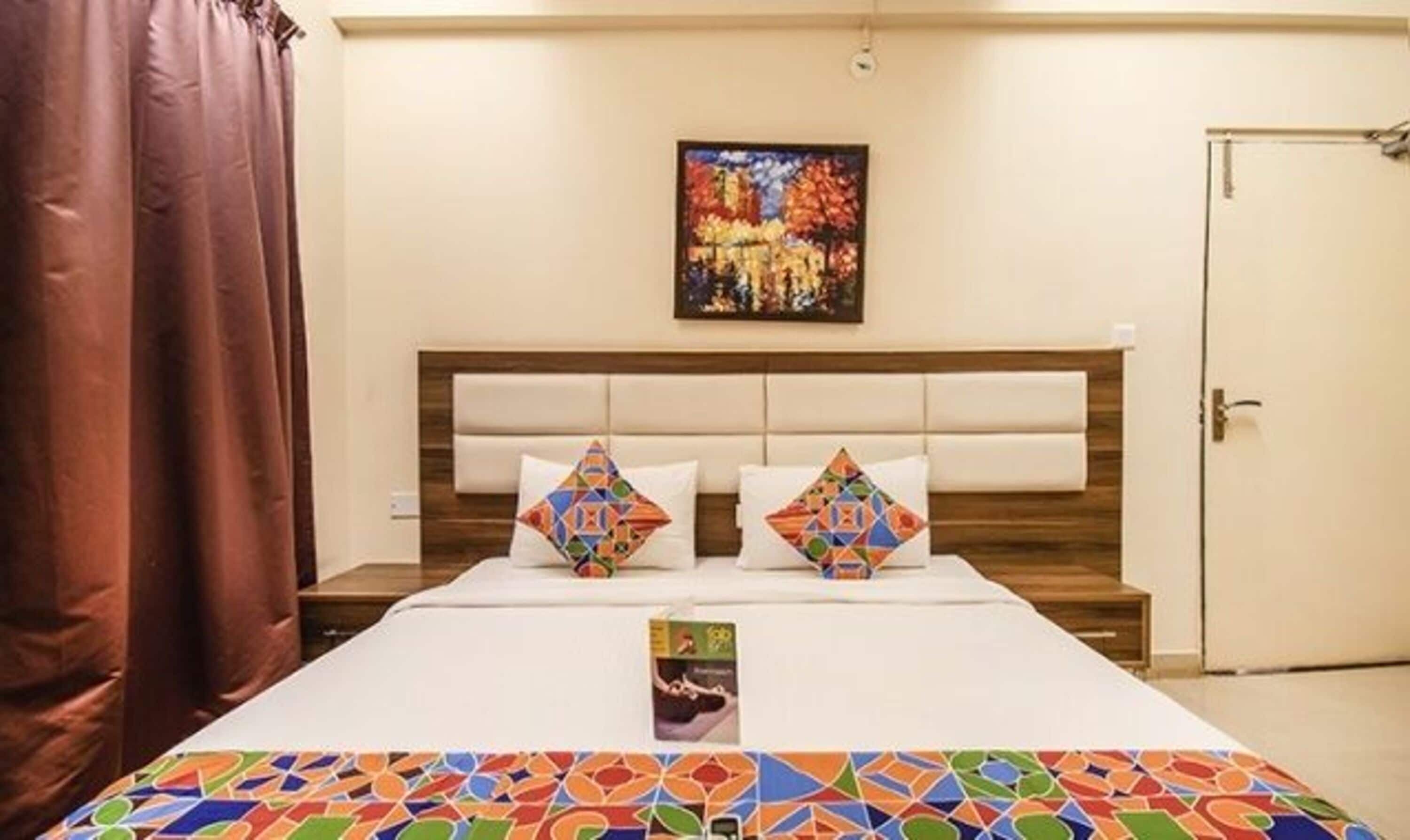 Een hotelkamer met een bed, twee kussens, een schilderij aan de muur en een deur.