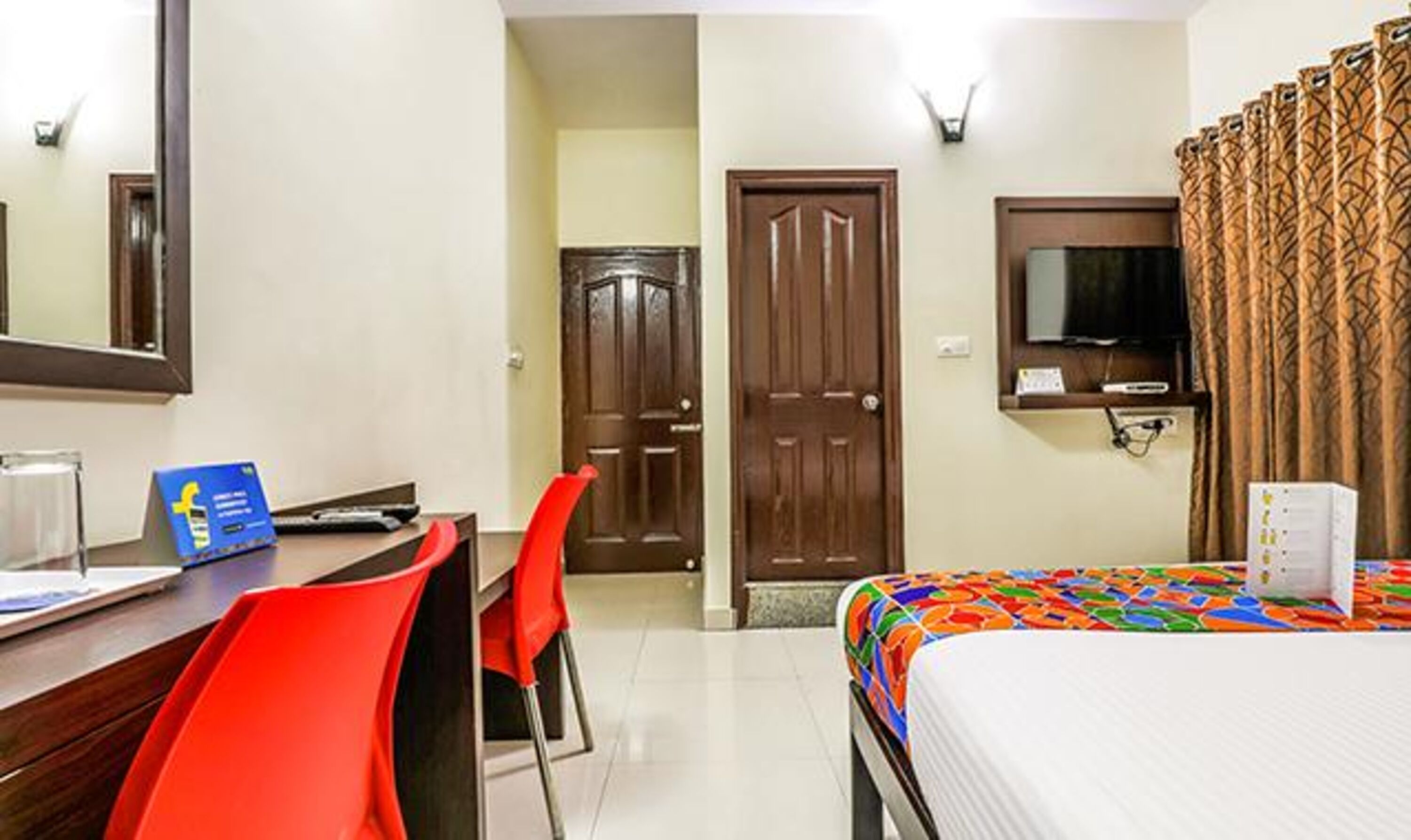 A hotel room with a bed, a desk with a chair, a television, and a door.
