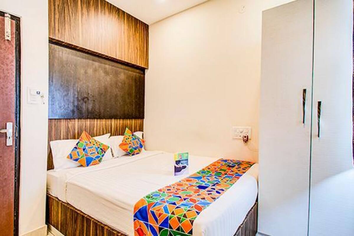 A hotel room with a bed, a wooden headboard, a white wall, and a door.