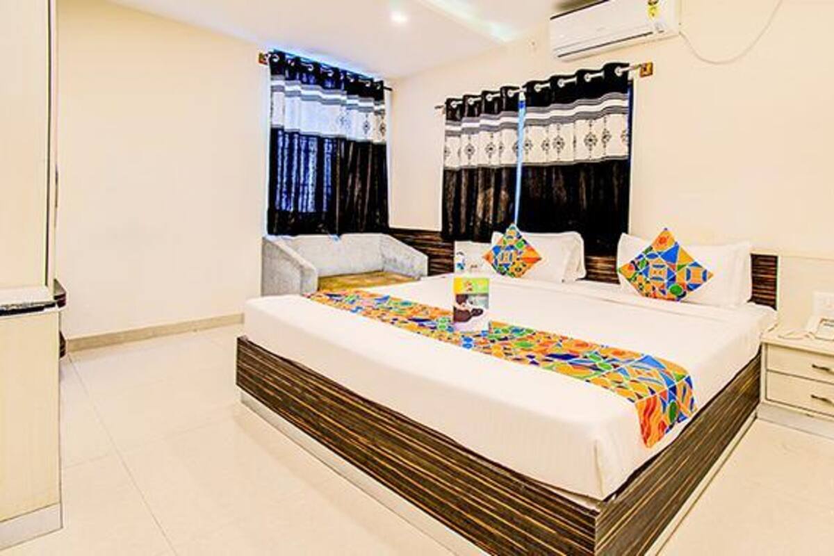 A hotel room with a large bed, a bedside table, a chair, and a window with curtains.