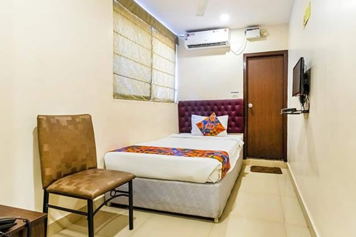 Un dormitorio pequeño y ordenado con una cama individual, una silla, un televisor y un equipo de aire acondicionado.