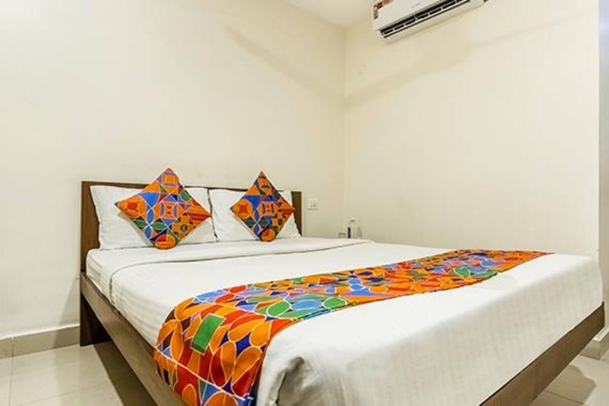 Habitación de hotel con una cama, dos almohadas, una manta colorida y un equipo de aire acondicionado en la pared.