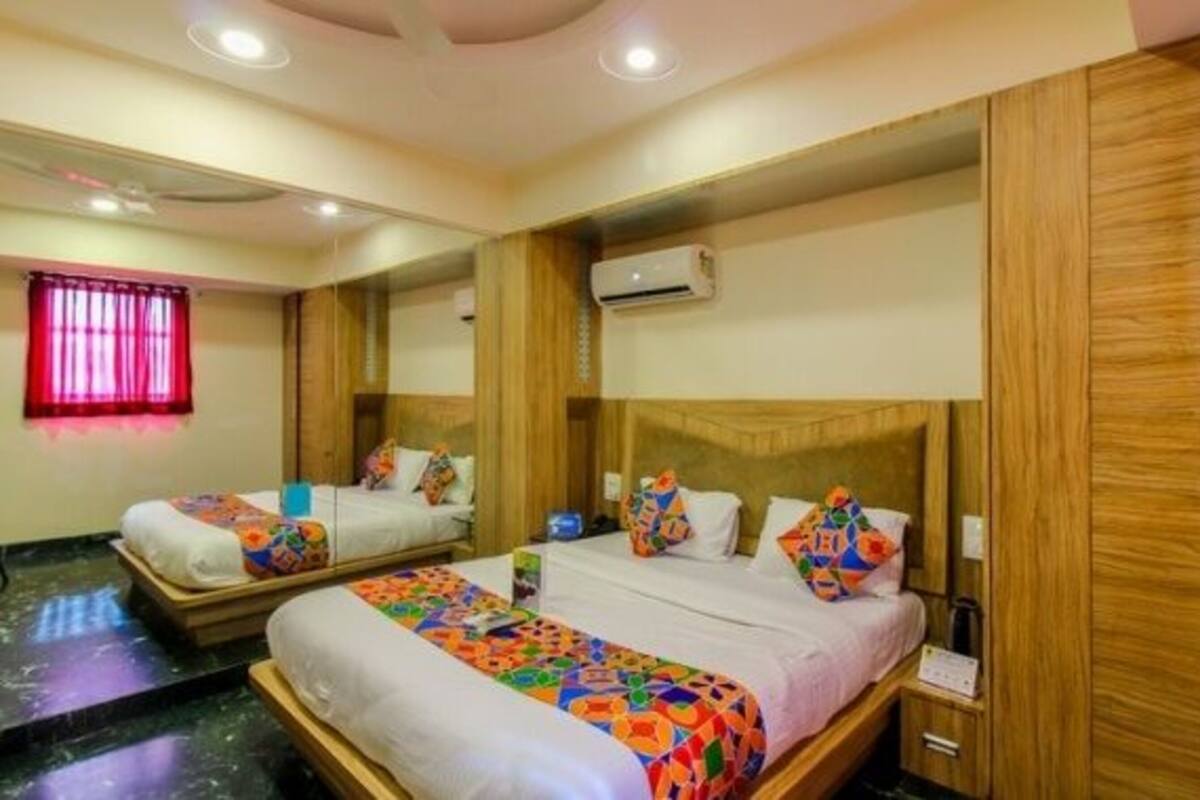 Quarto de hotel com duas camas, cabeceiras de madeira, cortina vermelha e um aparelho de ar condicionado.