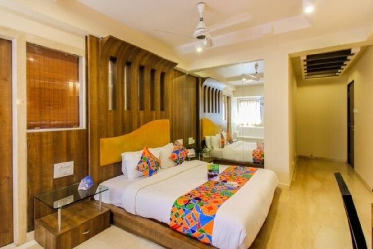 Quarto com cabeceira de madeira, mesa de cabeceira de vidro, cama com roupa de cama colorida e ventilador de teto.
