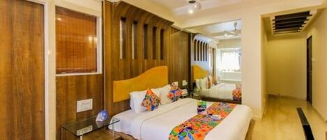 Un dormitorio con cabecera de madera, mesita de noche de cristal y ropa de cama colorida, además de un ventilador de techo.