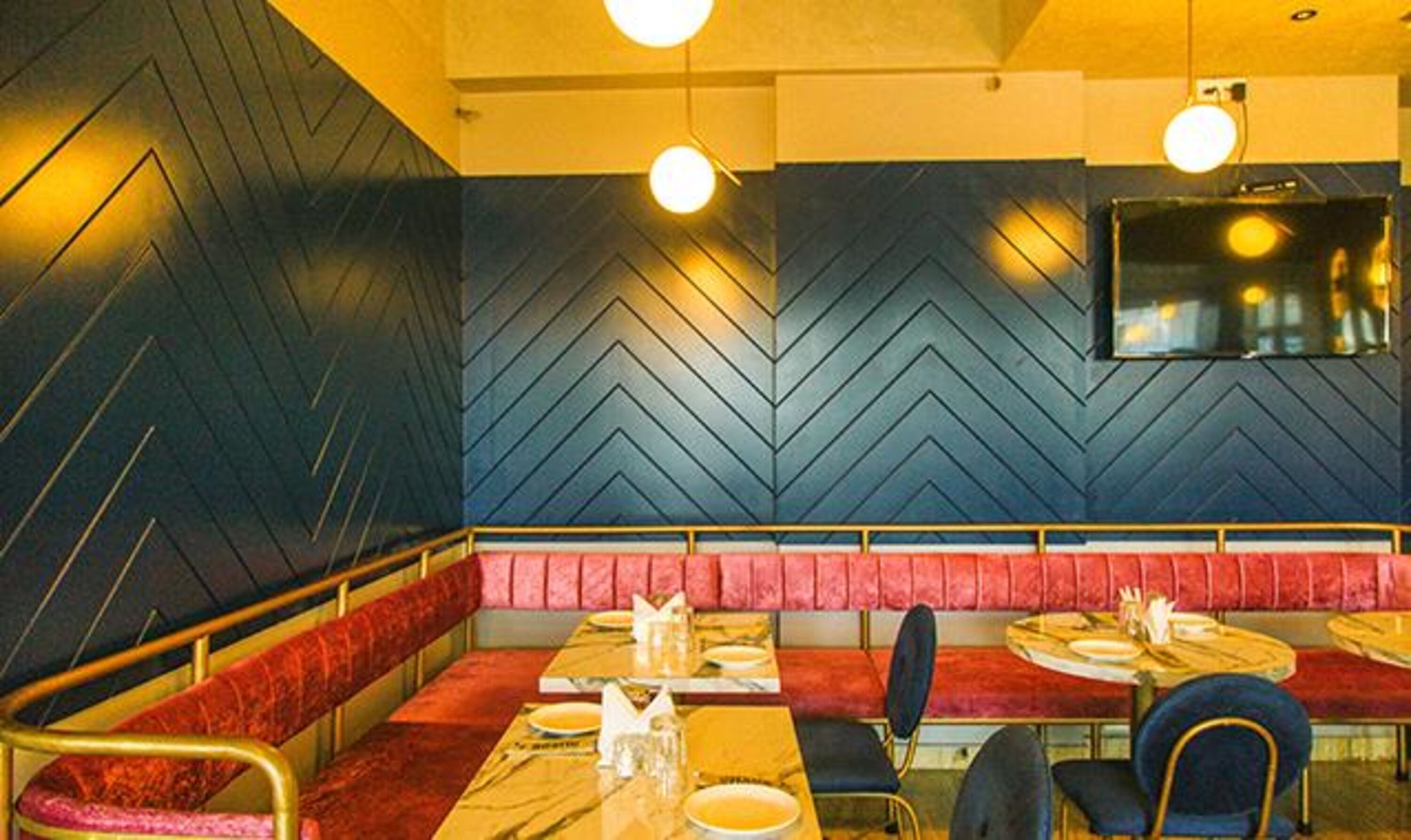 A restaurant interior with a chevron-patterned wall, red cushioned booths, and round tables with chairs.