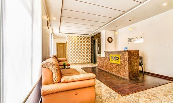 A hotel lobby with a reception desk, a seating area with a sofa, and a patterned wall.