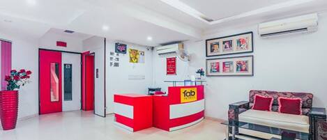 A hotel reception area with a red and white color scheme, a reception desk, a sofa, and framed artwork on the wall.