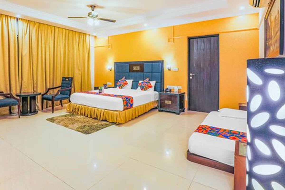 A hotel room with a bed, two chairs, a small table, a nightstand, and a door.