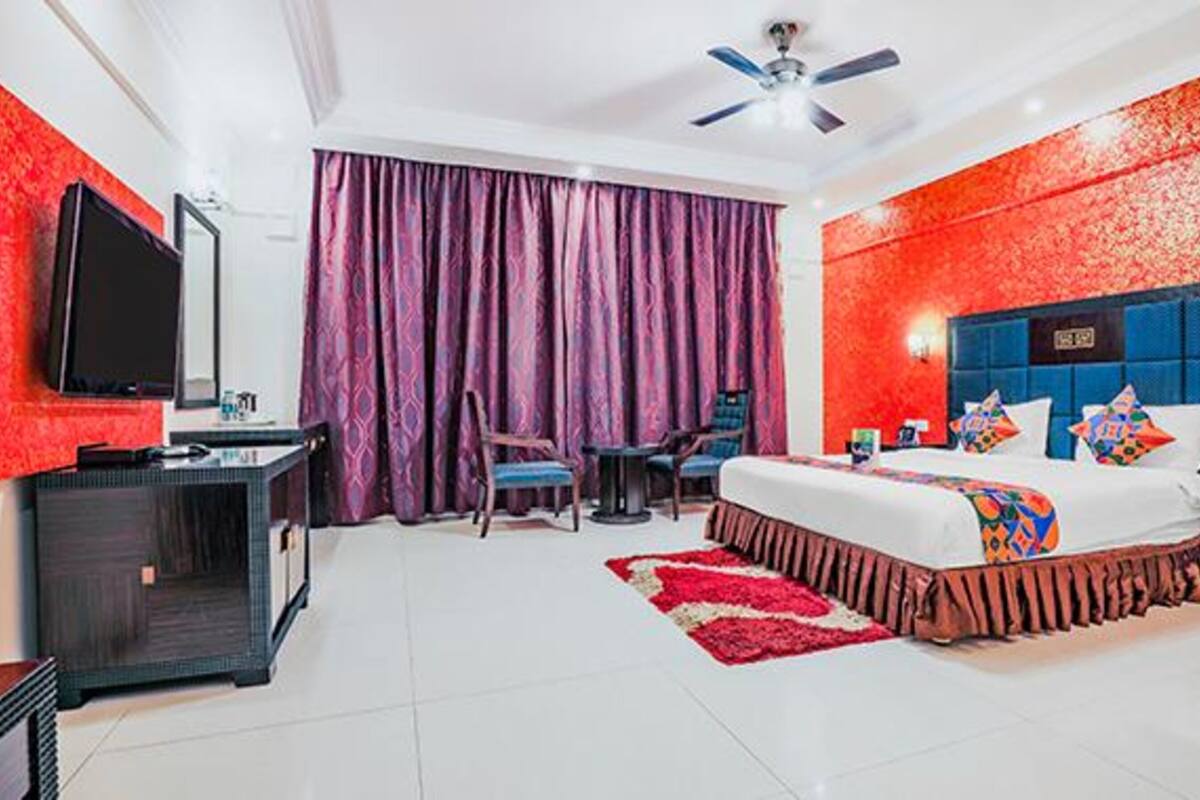 A hotel room with a bed, a desk, a chair, a television, and a ceiling fan.