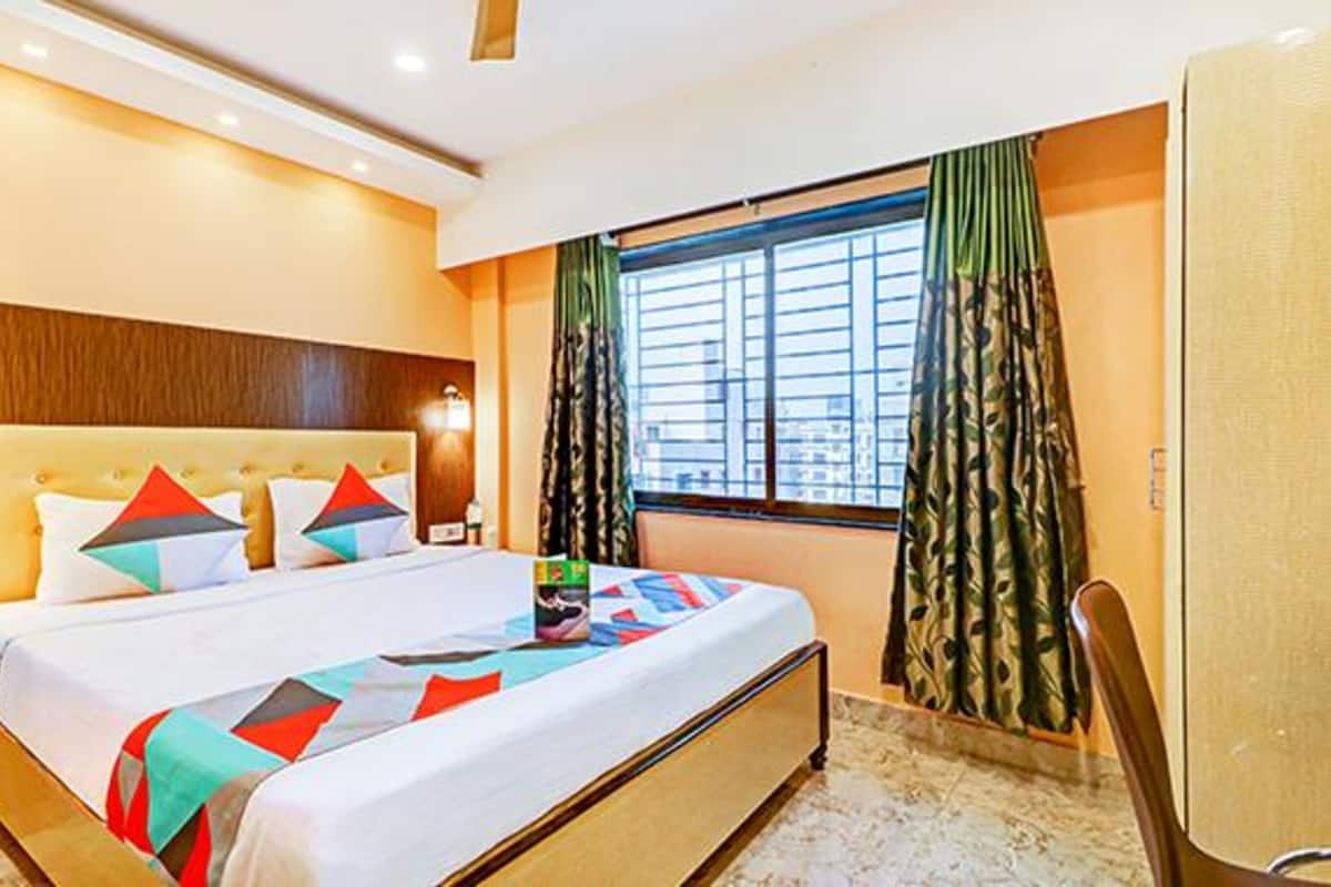 Habitación de hotel con una cama grande, cabecera, ventana con cortinas y un escritorio con silla.