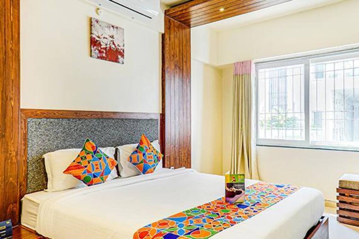 Une chambre d’hôtel avec un grand lit, une tête de lit en bois, une fenêtre avec des stores et un couvre-lit aux couleurs vives.