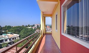 A narrow balcony with a metal railing, a large window, and a view of a cityscape with greenery. - Fabexpress Bzoy Inn (Dehradun)