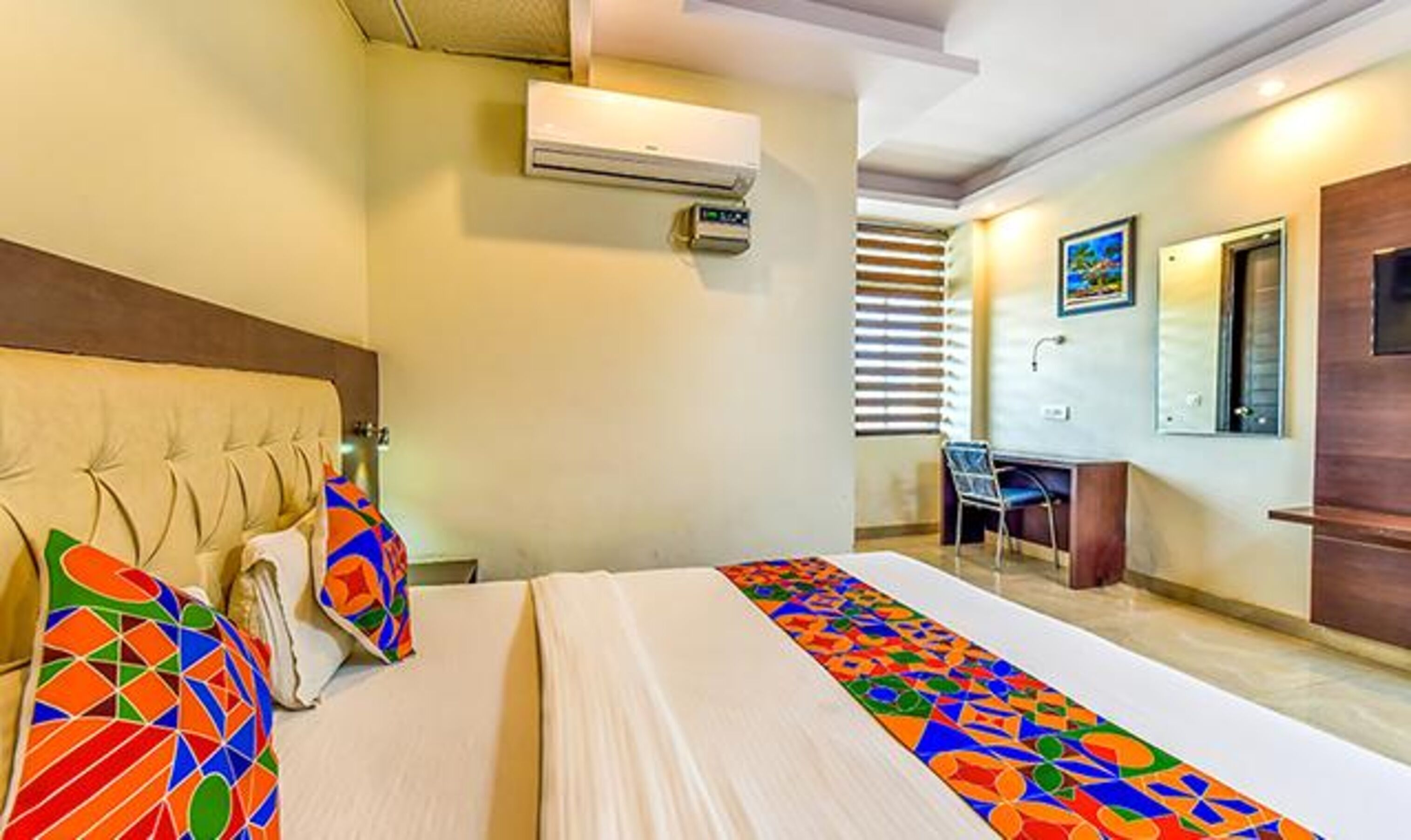 A hotel room with a bed, an air conditioning unit, a desk, and a chair.