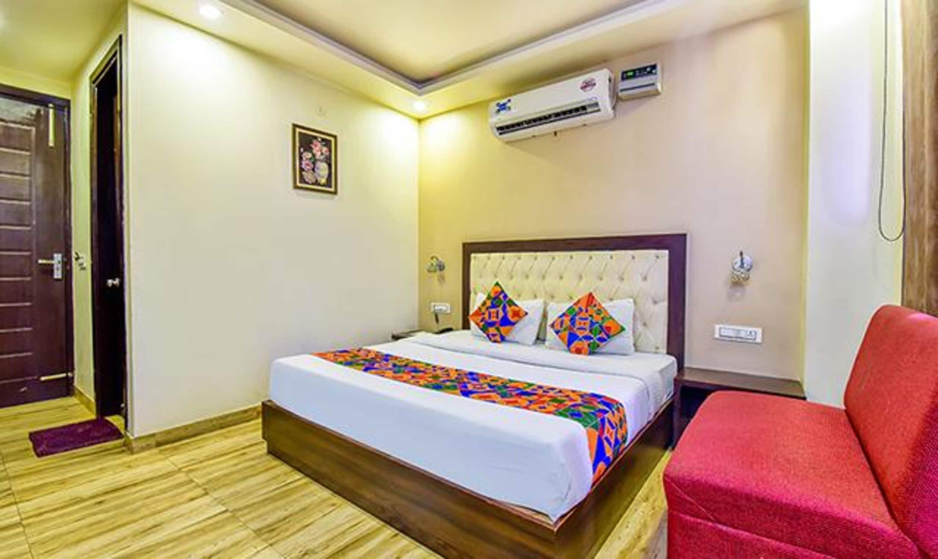 A hotel room with a bed, a red chair, an air conditioning unit, and a door.