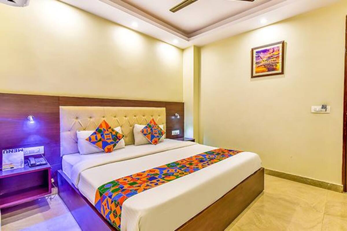 Una habitación de hotel con cama, mesita de noche, un cuadro en la pared y una puerta.