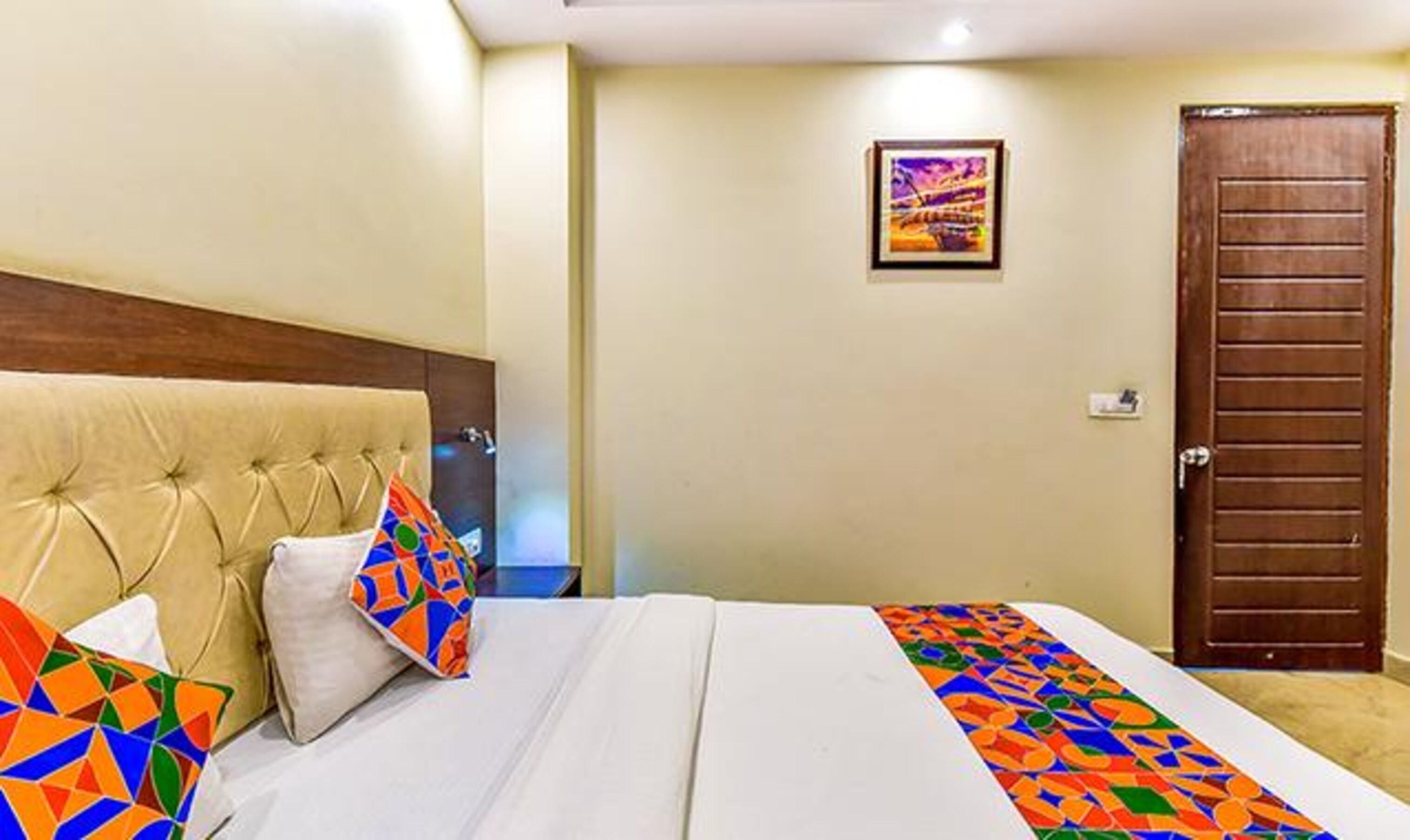 A hotel room with a bed, a headboard, a door, and a framed picture on the wall.