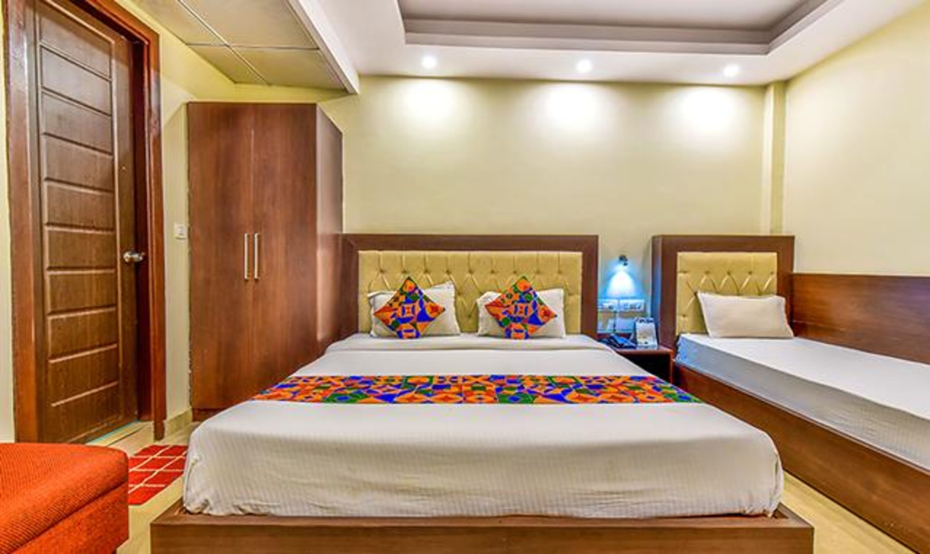 A hotel room with two beds, a wardrobe, and a nightstand with a lamp.