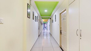 A long, narrow hallway with white walls and a green ceiling. There are framed pictures on the walls and a door on the right side.
