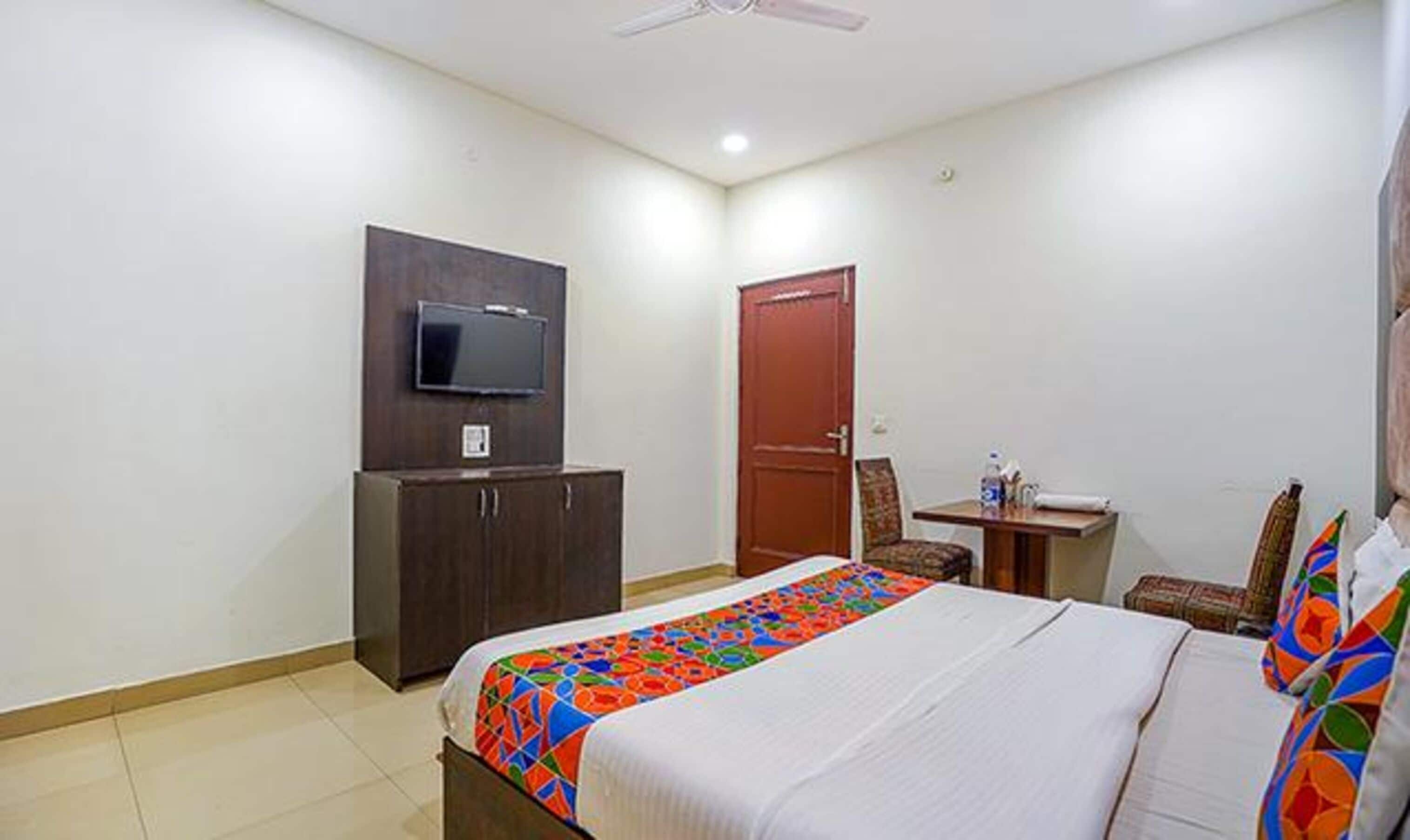 A hotel room with a bed, a desk, a chair, a television, and a wardrobe.