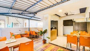 A modern dining area with orange chairs and tables, a colorful floor, and a ceiling with exposed beams. - Fabexpress A1 Dalcha (Pune)