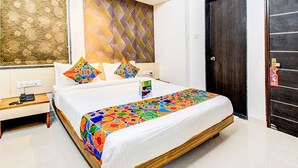 A hotel room with a bed, a nightstand, a wall with patterned wallpaper, and a door. - Fabexpress A1 Dalcha (Pune)