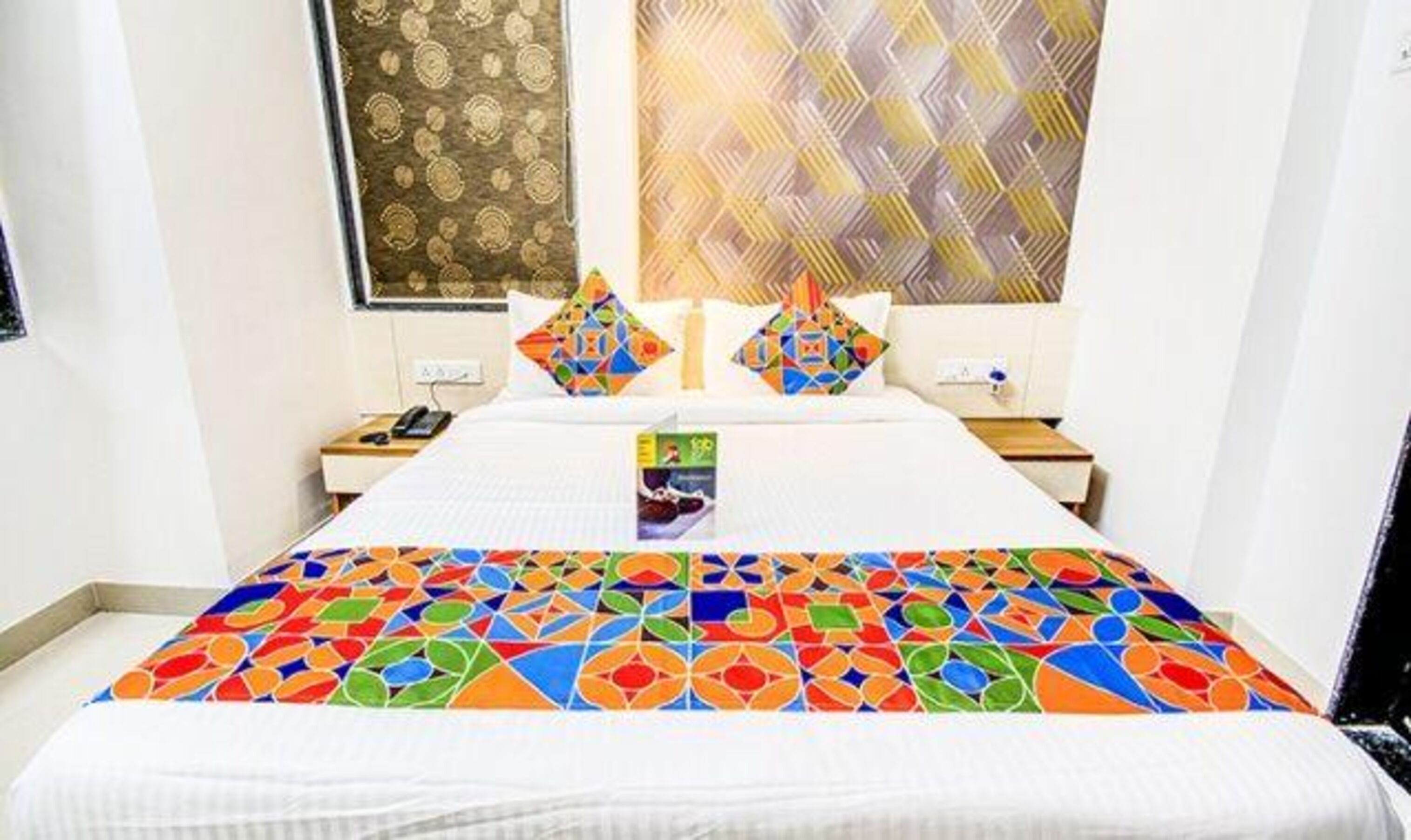 Ein Hotelzimmer mit einem großen Bett, zwei Nachttischen, einem Wandtelefon und einem gerahmten Kunstwerk über dem Bett.