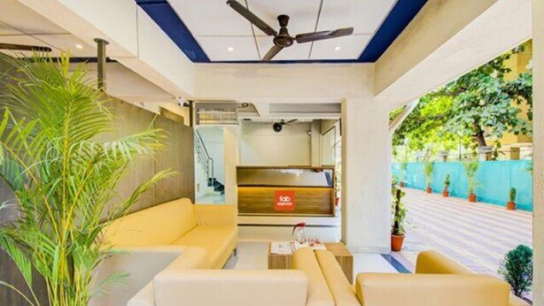 A hotel lobby with a ceiling fan, a reception desk, and a seating area with a large plant. - Fabexpress A1 Dalcha (Pune)