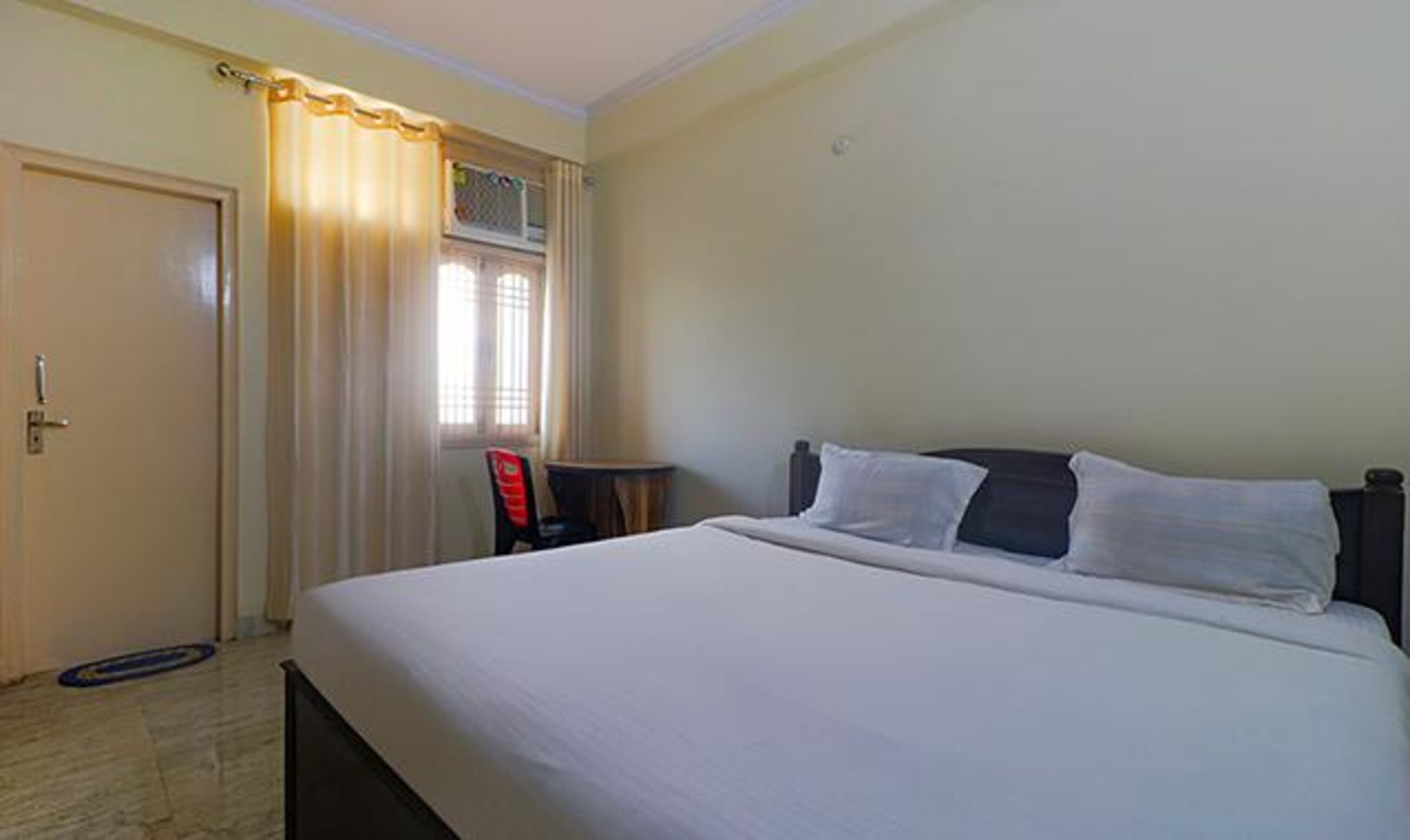 Une chambre d’hôtel avec un lit, une chaise, une petite table et une porte.