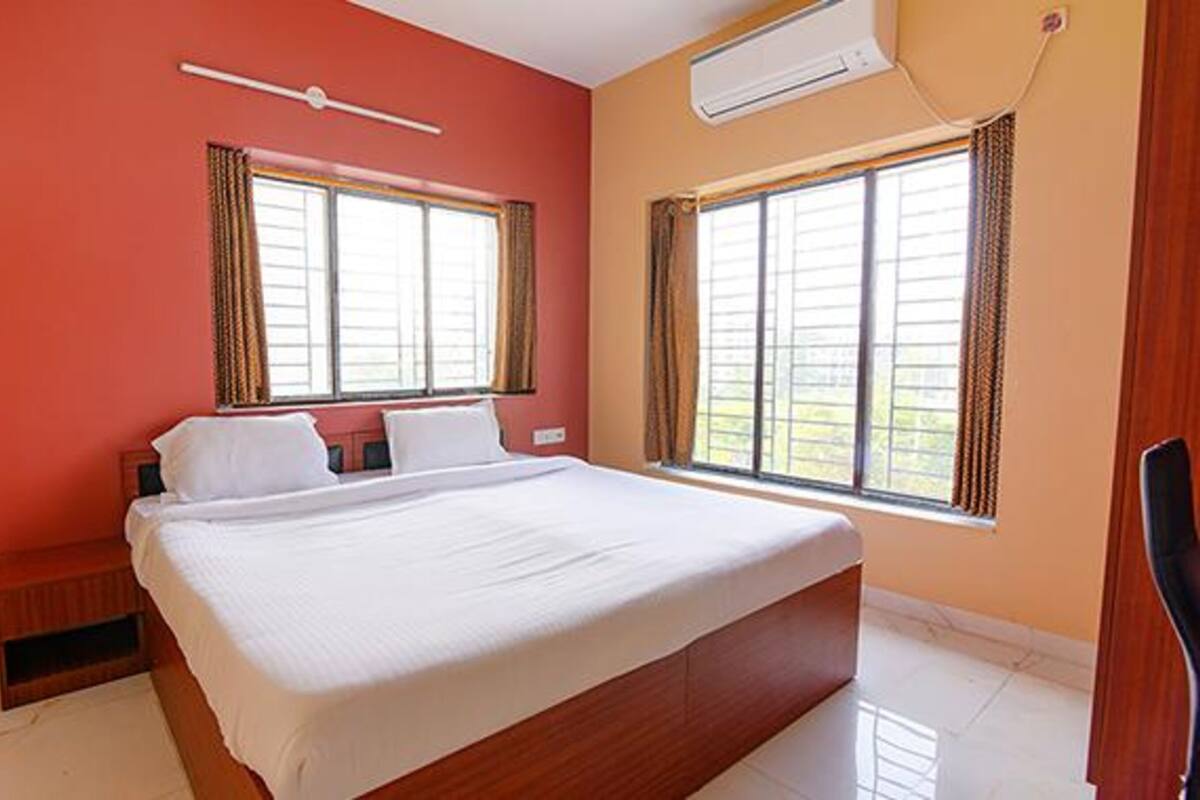 A hotel room with a large bed, two windows, and an air conditioning unit.