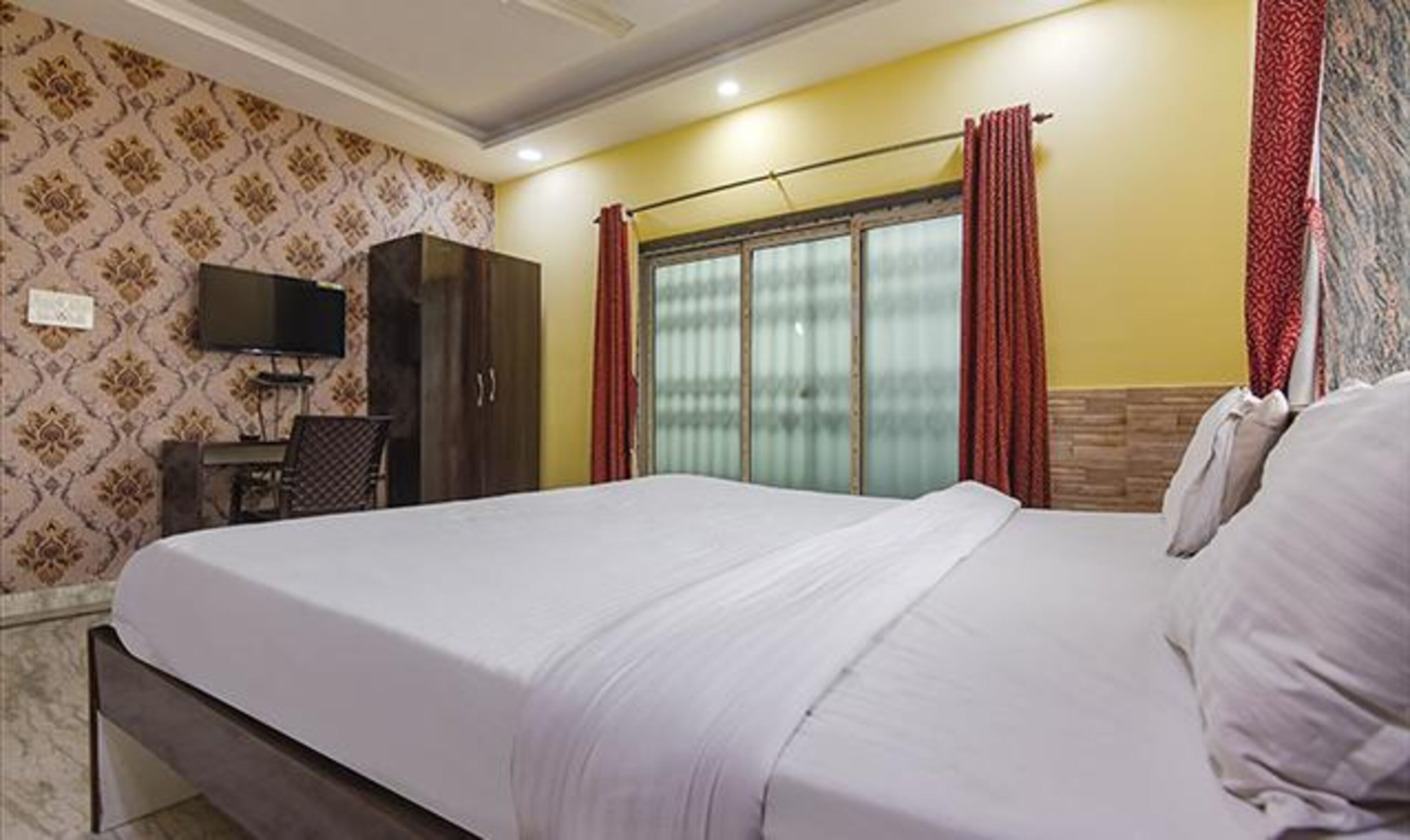 Habitación de hotel con una cama grande, televisión montada en la pared, armario y ventana con cortinas.