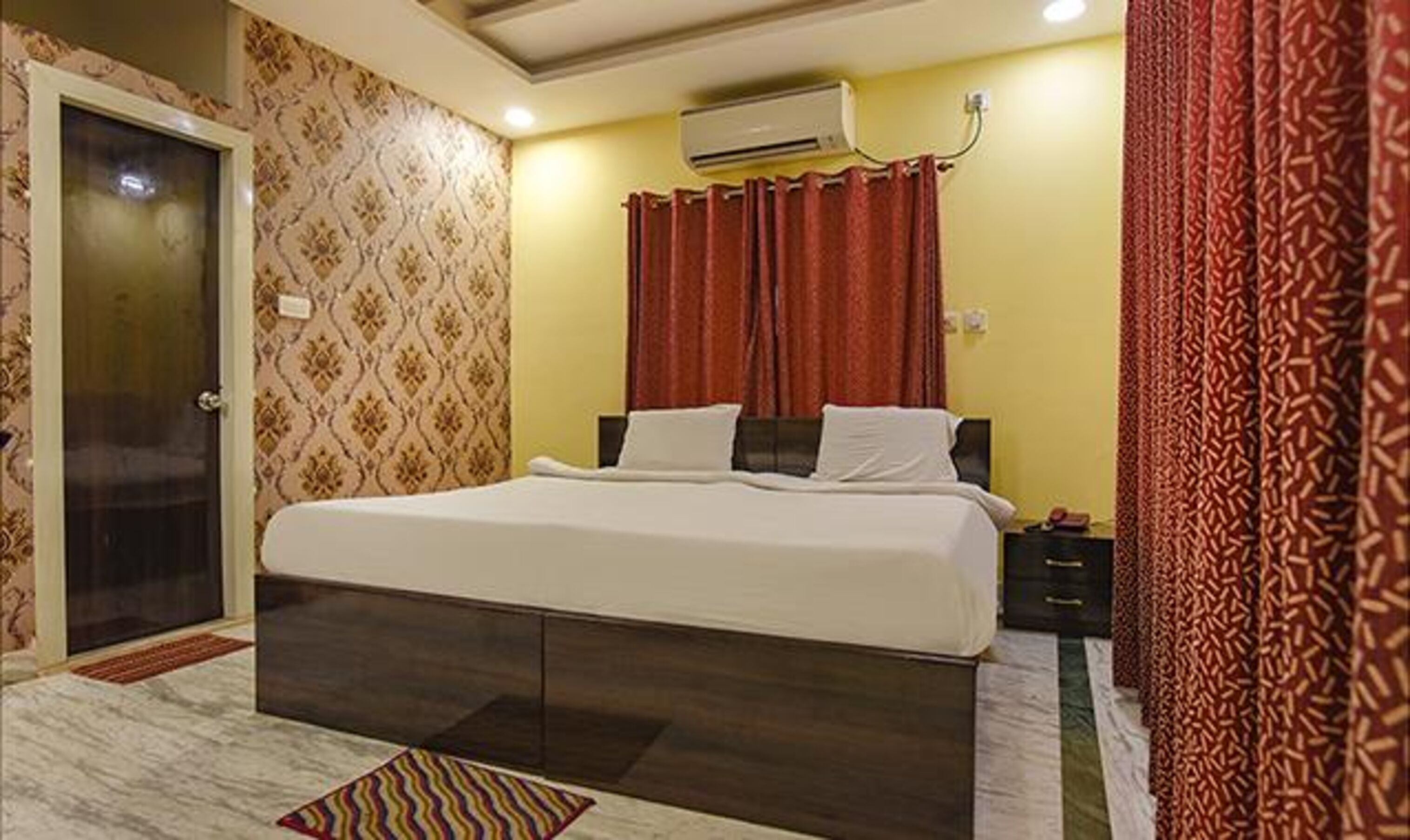 Quarto de hotel com cama, mesa de cabeceira, aparelho de ar condicionado e cortina estampada.