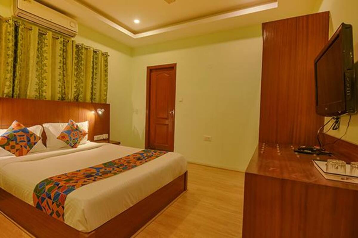 A hotel room with a large bed, a wooden headboard, a desk with a flat-screen TV, and a door.