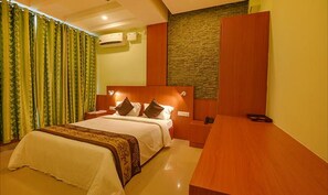 A hotel room with a large bed, a wooden nightstand, a desk, and a stone accent wall. - Fabhotel Jen & Jo (Bengaluru)