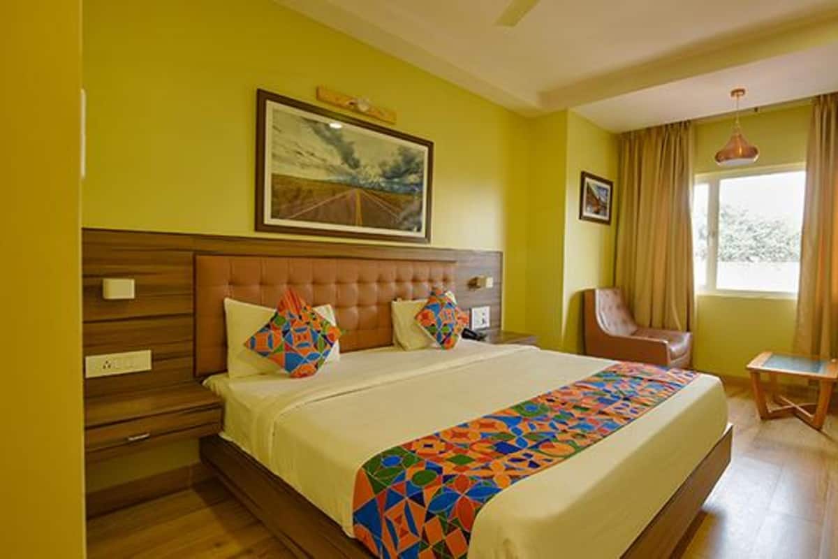 A hotel room with a large bed, a chair, a small table, and a painting on the wall.