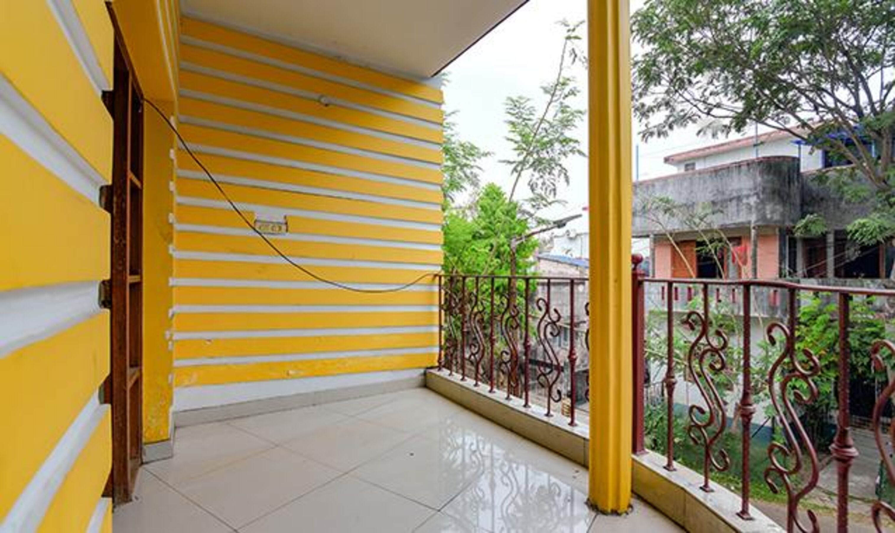 A balcony with yellow and white striped walls, a tiled floor, and a metal railing.