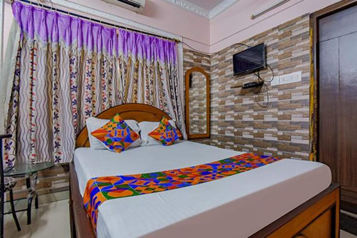 A neatly made bed with a colorful blanket, a wooden headboard, and a TV mounted on a brick wall.